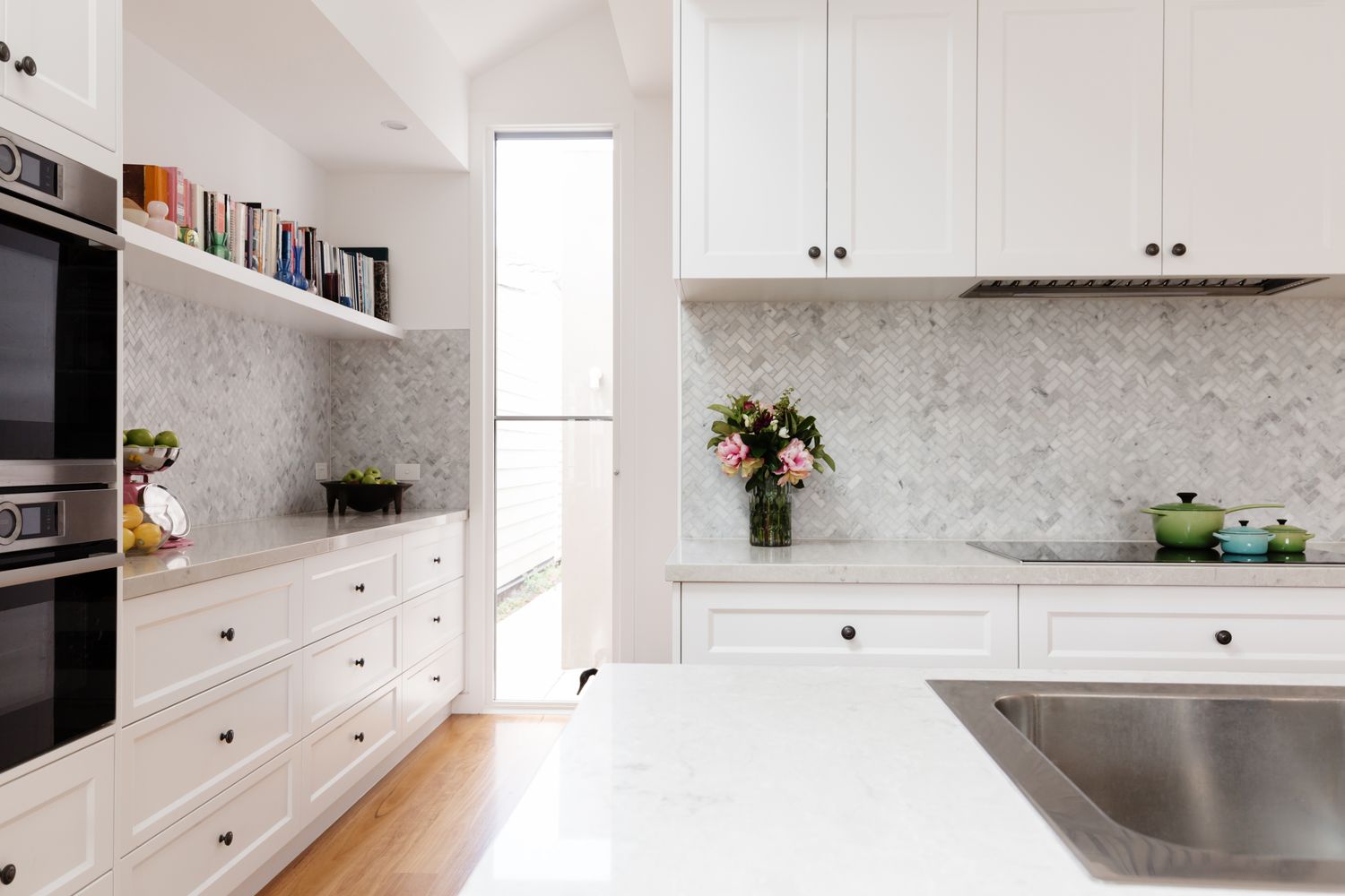 Modern kitchen with white cabinetry marble backsplash builtin appliances and decor on the counter