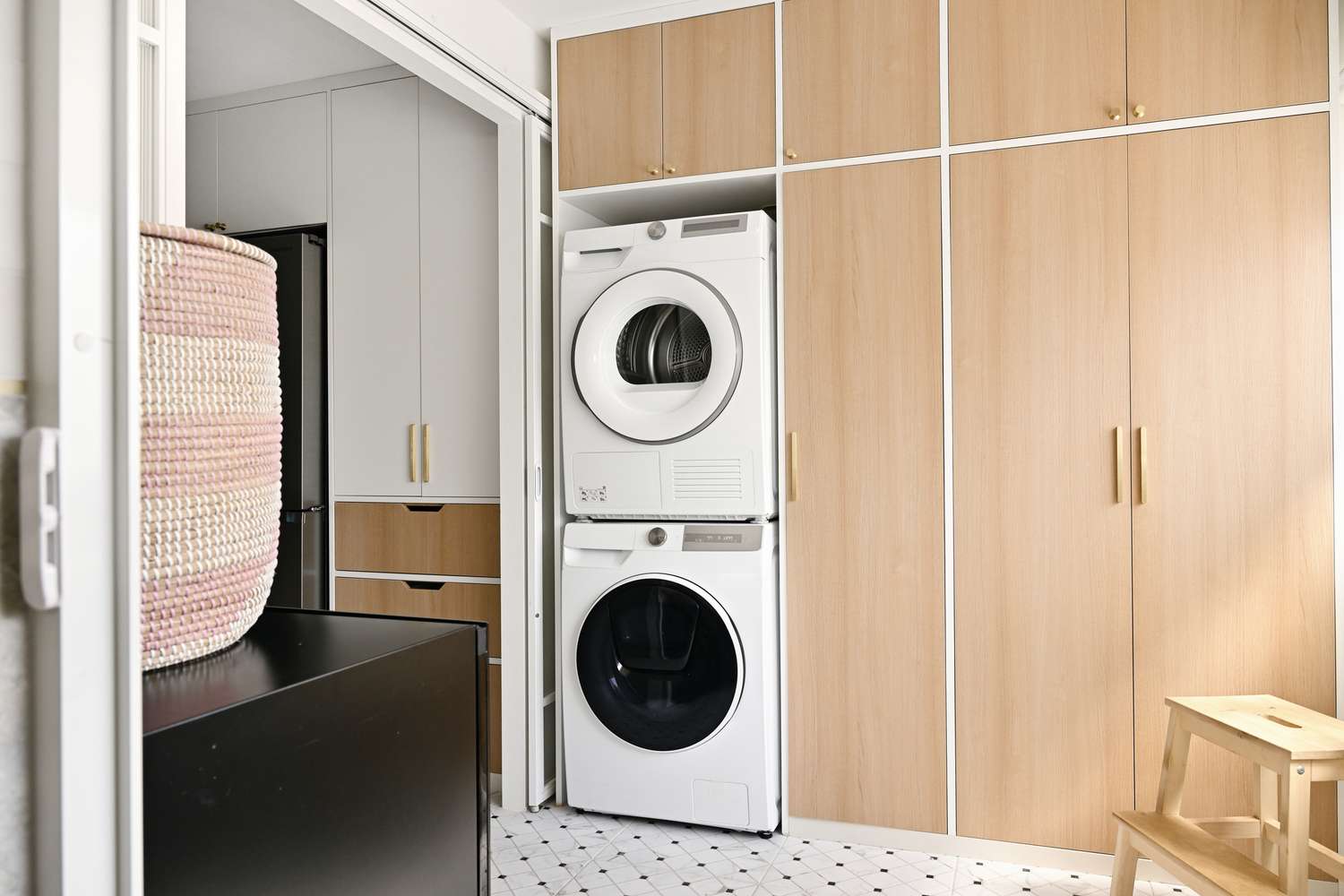A laundry area with a washer and dryer stacked vertically surrounded by wooden cabinets