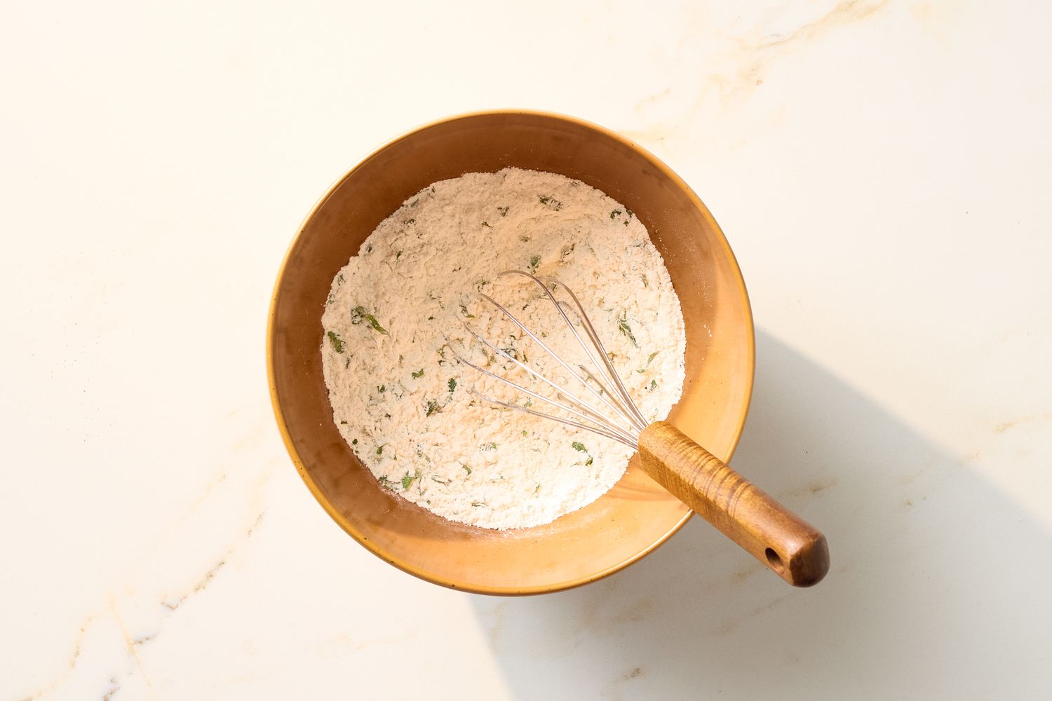 Mixing bowl with flour and herbs whisk inside