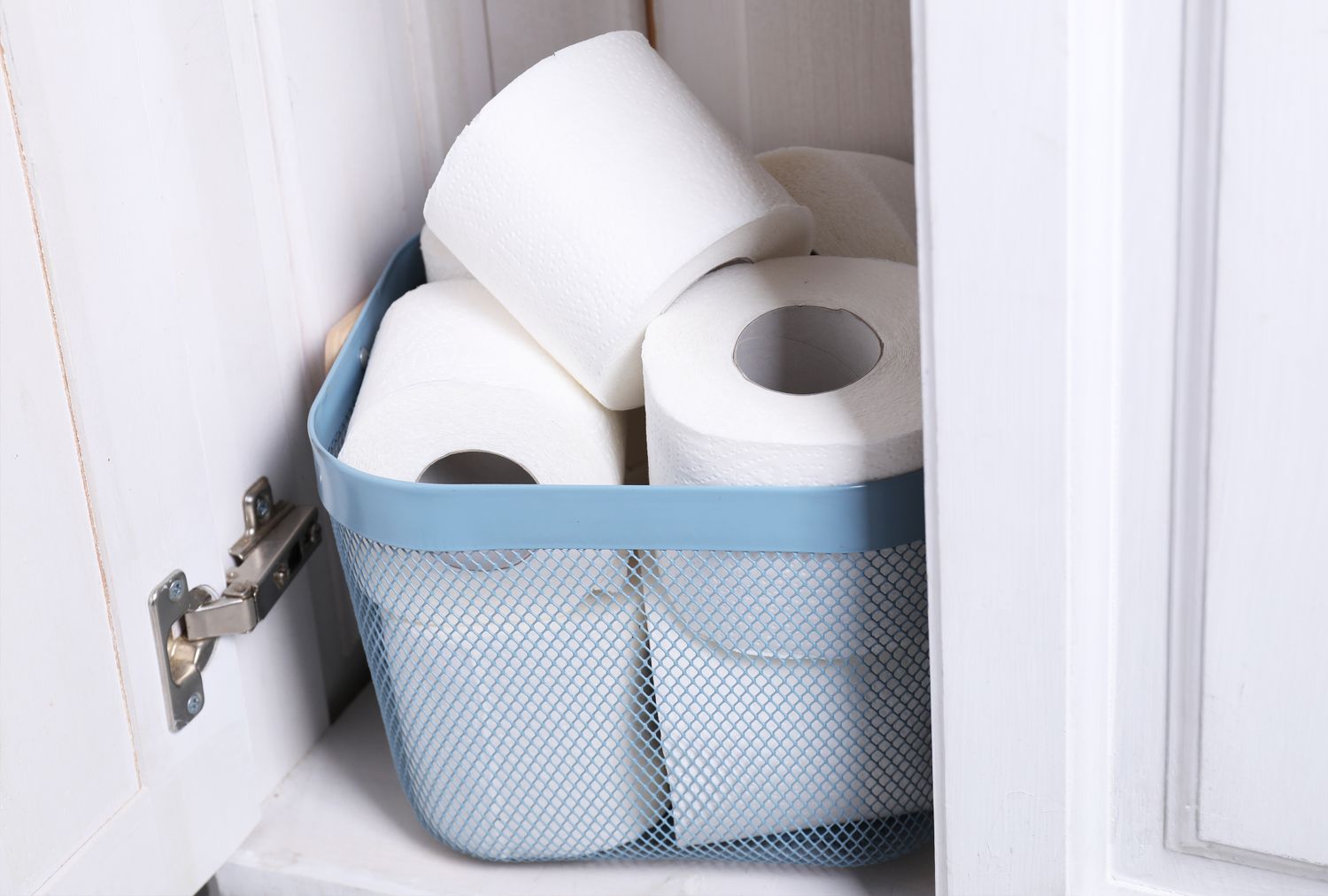 A blue basket containing rolled toilet paper inside a cabinet
