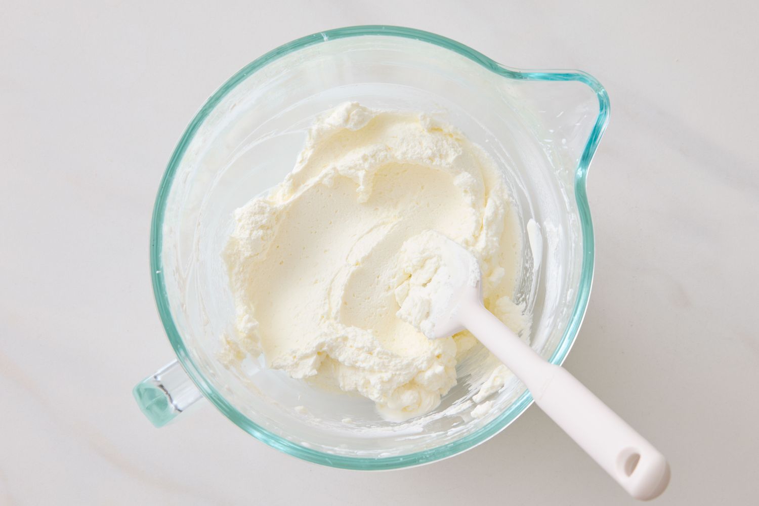 A glass bowl with creamy vanilla ice cream and a white spatula