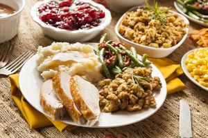 Plate with turkey mashed potatoes stuffing green beans cranberries and corn with additional bowls in the background