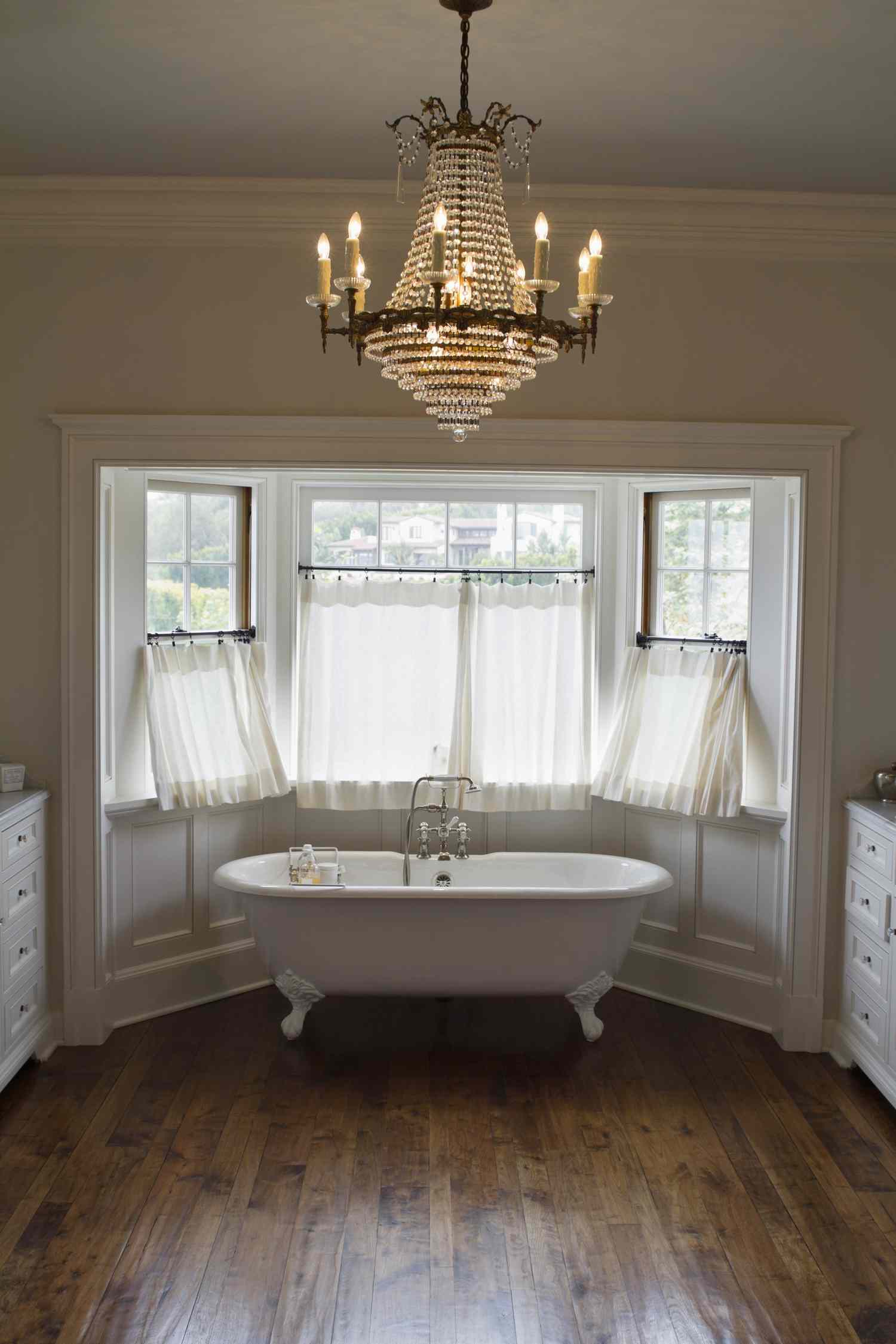 A bathroom with a clawfoot tub large windows and a chandelier