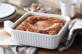 A baked dessert in a square dish on a table with mugs and plates nearby