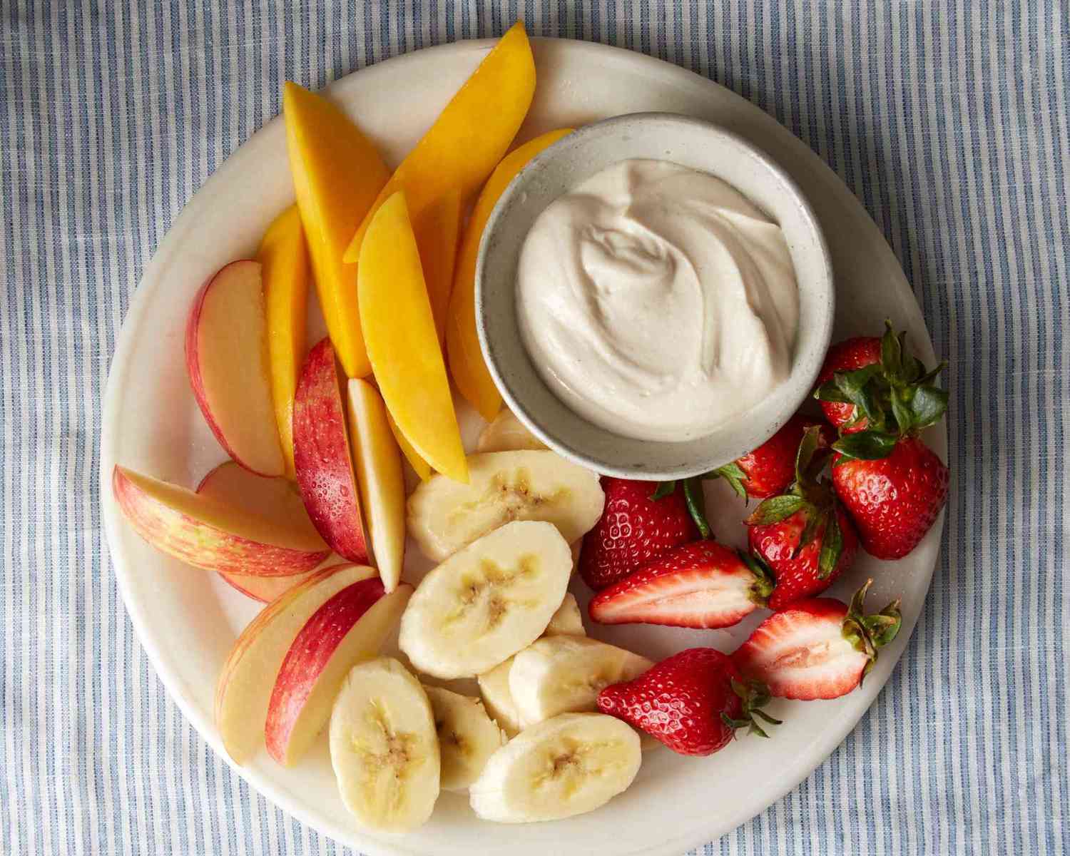 sliced strawberries, bananas, apples, and mango on plate with small bowl of dip