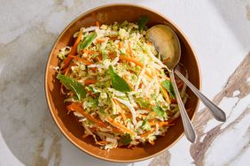 Bowl of napa cabbage slaw garnished with mint leaves and a serving spoon and fork placed inside the bowl