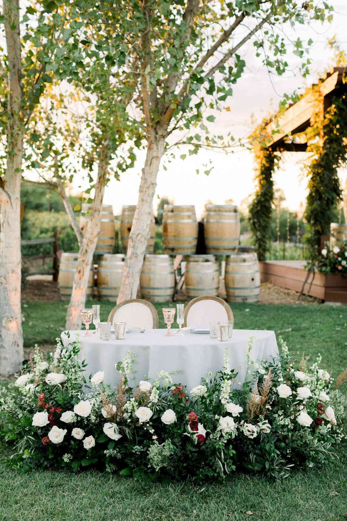 sweetheart table outdoor with barrels backdrop and roses around foot of table