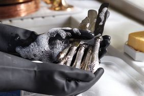 Hands wearing gloves cleaning silver utensils with soap suds