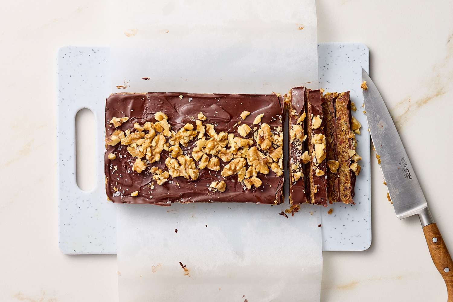 Sliced chocolate walnut dessert bar on a cutting board with a knife