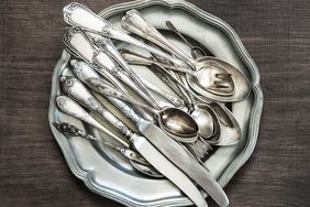 A stack of various utensils including spoons forks and knives on a plate