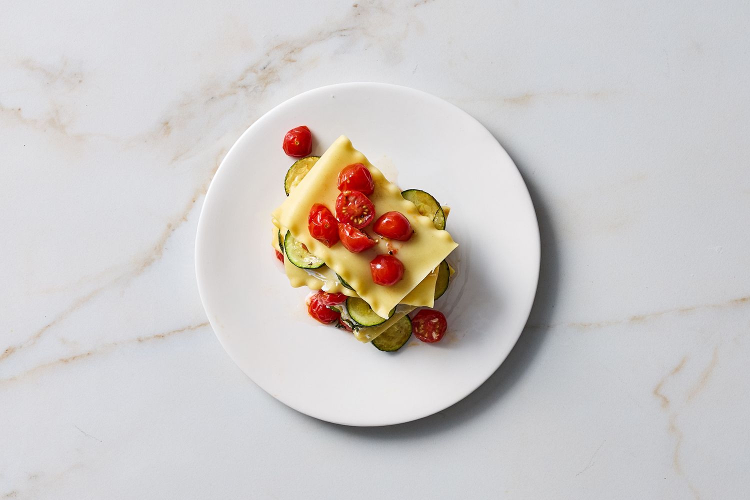 A serving of lasagna with zucchini slices and cherry tomatoes on a plate