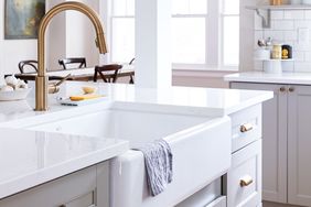 Farmhousestyle kitchen sink with a towel draped over the front surrounded by a bright kitchen with white countertops
