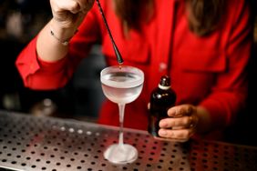 small droplet of liquid dripping from metal stick into cocktail glass on bar