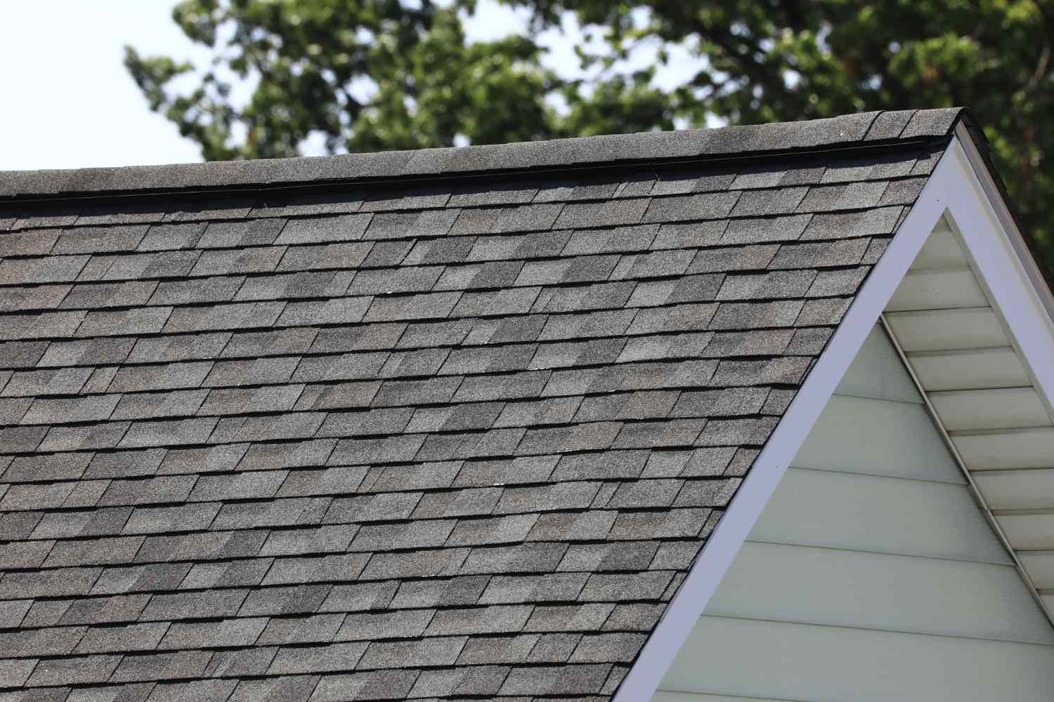Asphalt roof shingles on a gable roof trees in the background