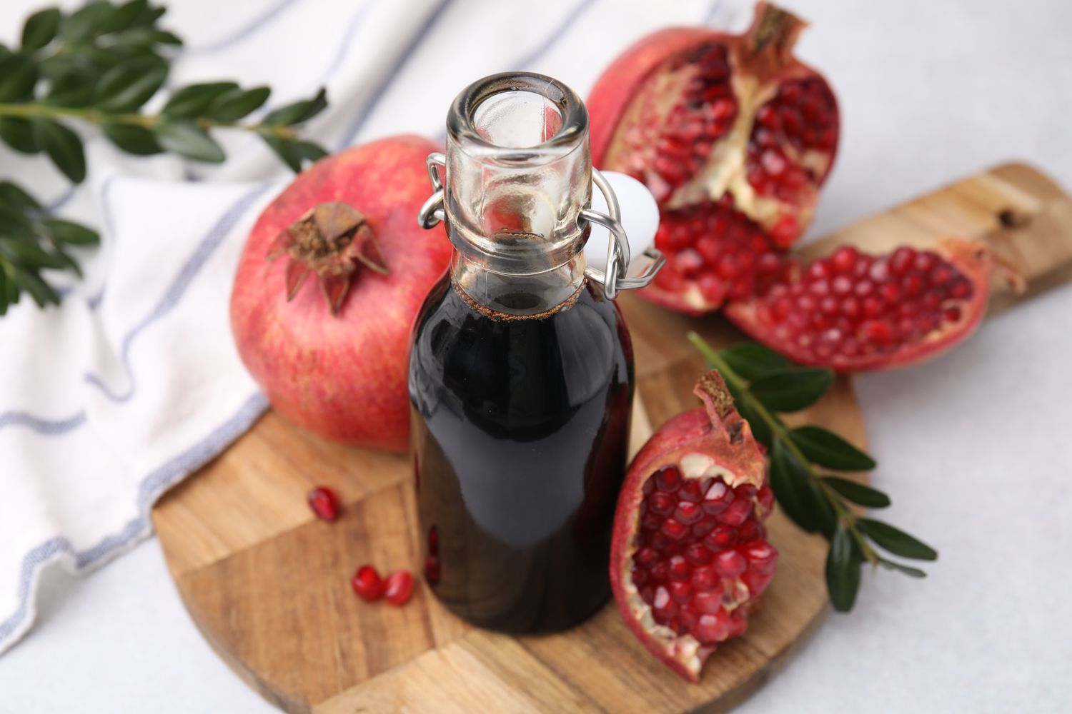 pomegranate molasses in glass bottle with pomegranate fruit and leaves on light surface