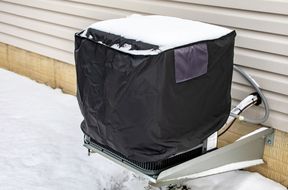 An outdoor HVAC unit covered with a protective cover surrounded by snow