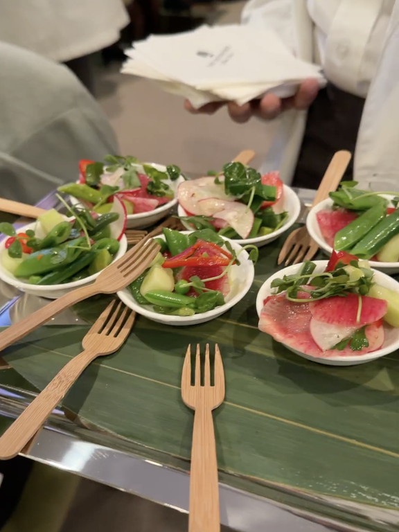 A tray with small bowls of salad garnished with vegetables each accompanied by a bamboo fork
