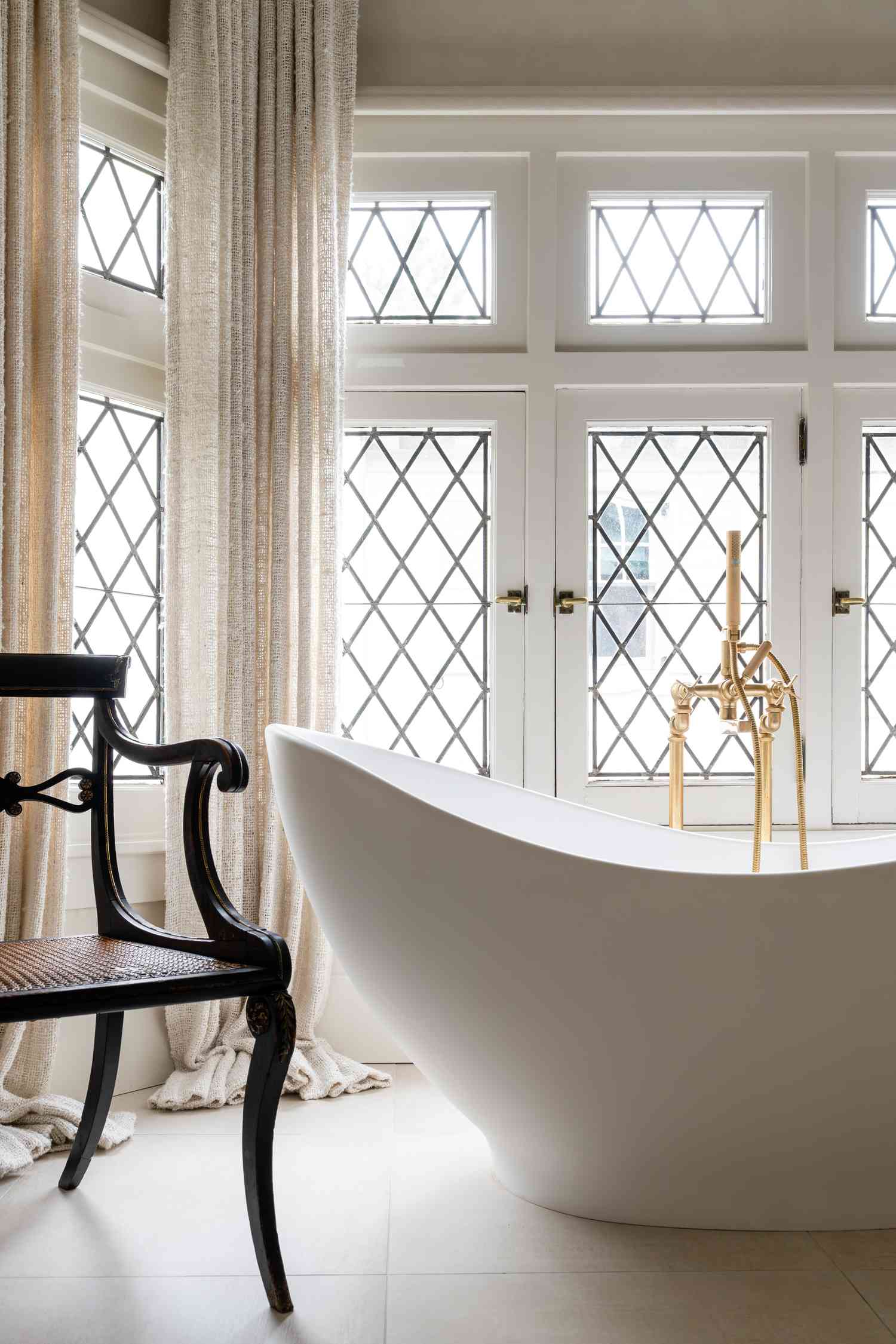 Freestanding bathtub and antique chair in a room with window designs
