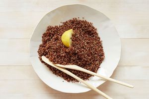 A plate of cooked red quinoa garnished with a lemon wedge and accompanied by two wooden utensils