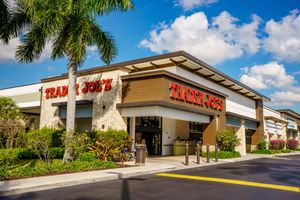 Front view of a Trader Joes store with palm trees and a clear sky in the background