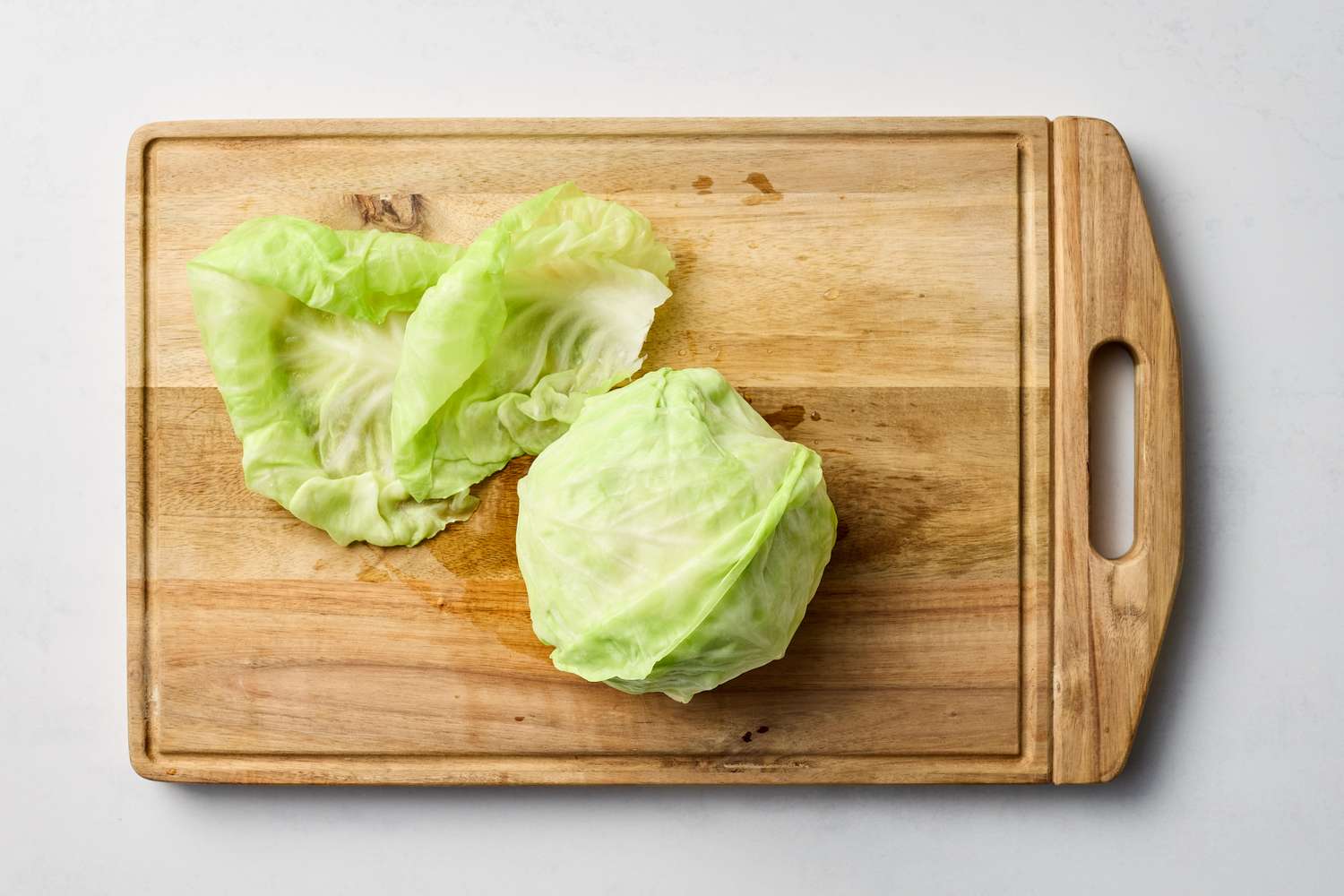 Cabbage leaves and a halved cabbage on a wooden cutting board