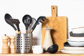 A collection of kitchen utensils in a holder and dishware on a wooden surface