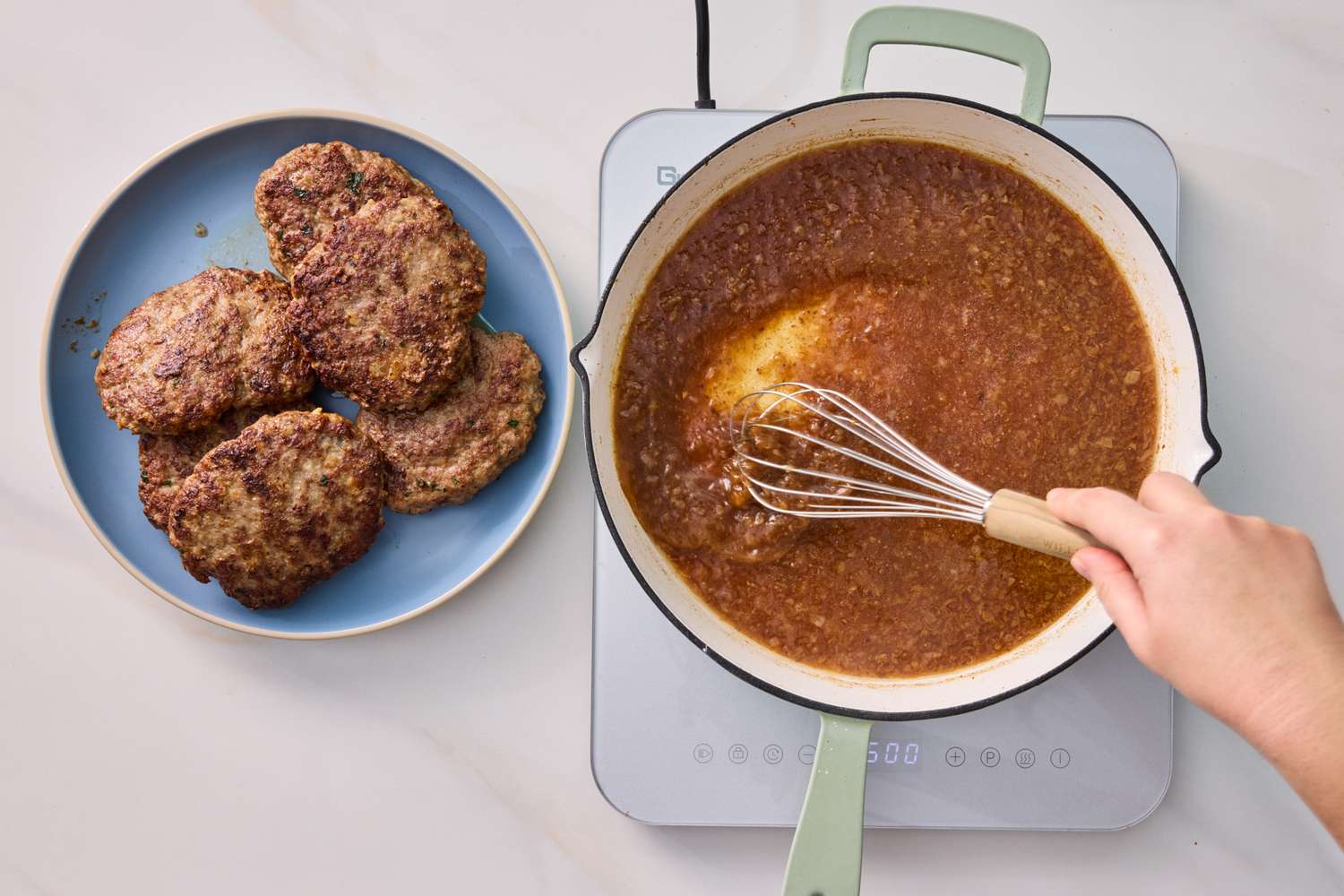 A person whisking onion gravy in a skillet next to a plate of cooked Salisbury steaks