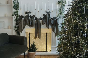 Christmas decorations featuring bows a lit tree and a mantel adorned with candles and greenery