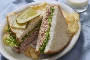 Ham salad sandwich with lettuce sliced pickles served with potato chips and a glass of milk on the side