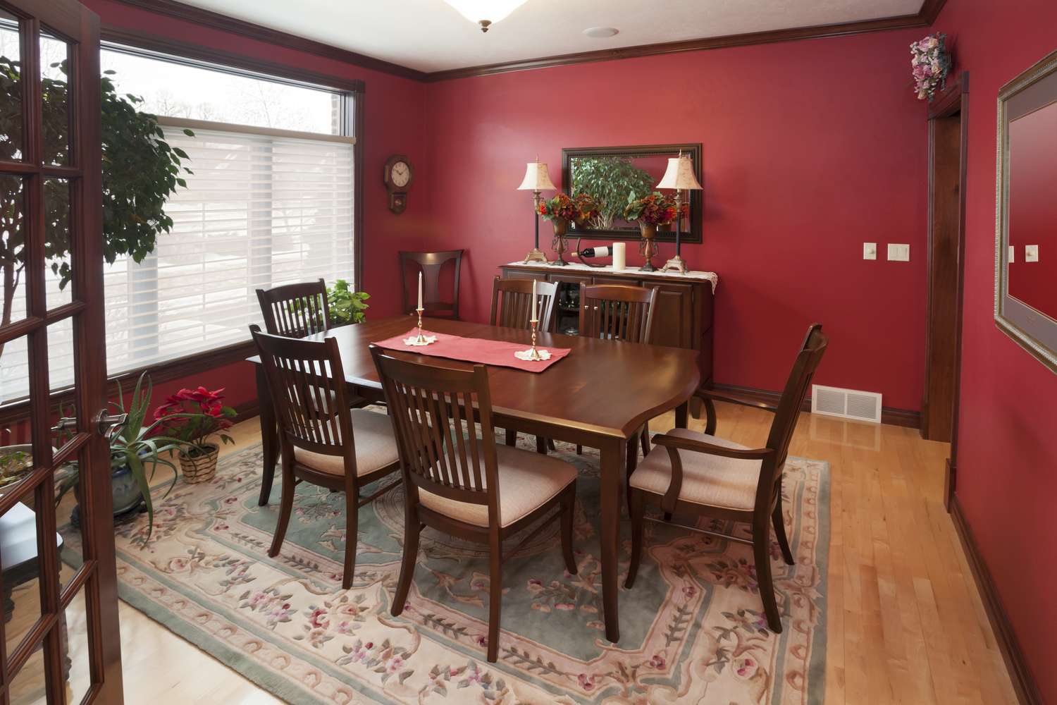 A dining room with a wooden table six chairs and a decorative setup including plants and a mirror