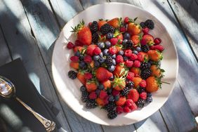 fresh strawberries, blueberries, raspberries, and blackberries on a white plate on a painted wooden surface
