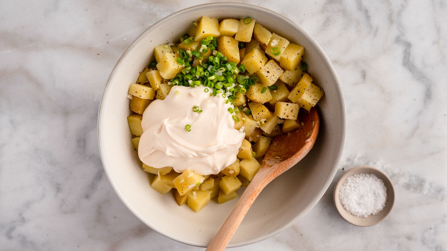 Adding mayonnaise and scallions to cooked cubed potatoes in a bowl