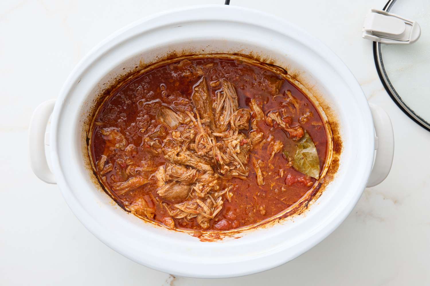 Slow cooker with pulled pork simmering in tomato-based sauce