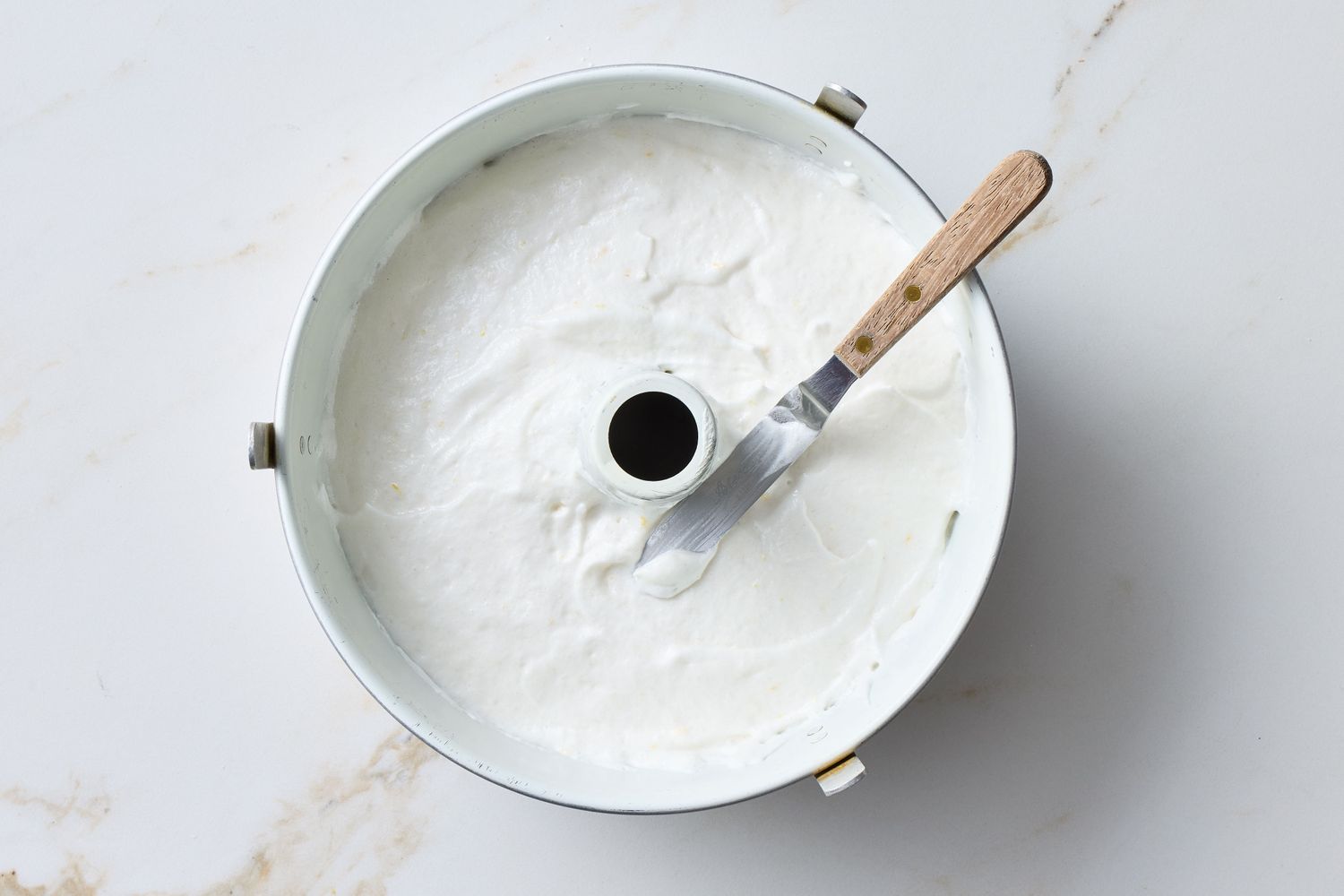 Angel food cake batter spread in a tube pan with a spatula resting on the edge