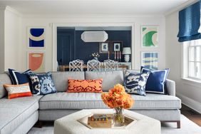 A living room with a sectional sofa decorative pillows a coffee table with flowers and a view of a dining area in the background