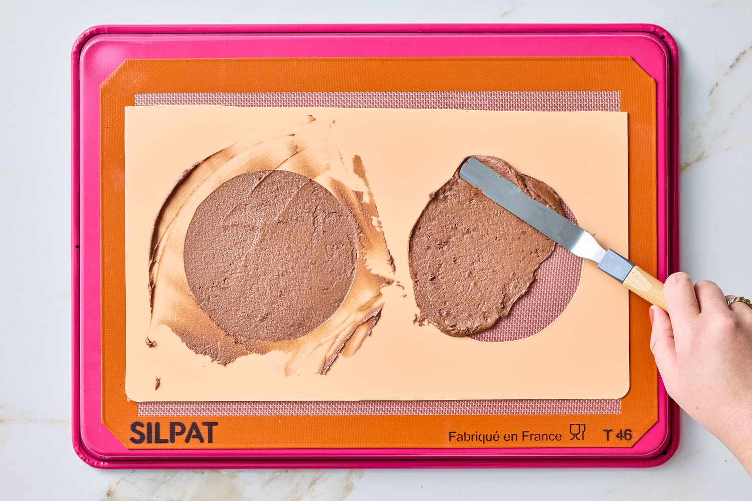 A spatula spreading chocolate mixture on a Silpat baking mat placed on a tray
