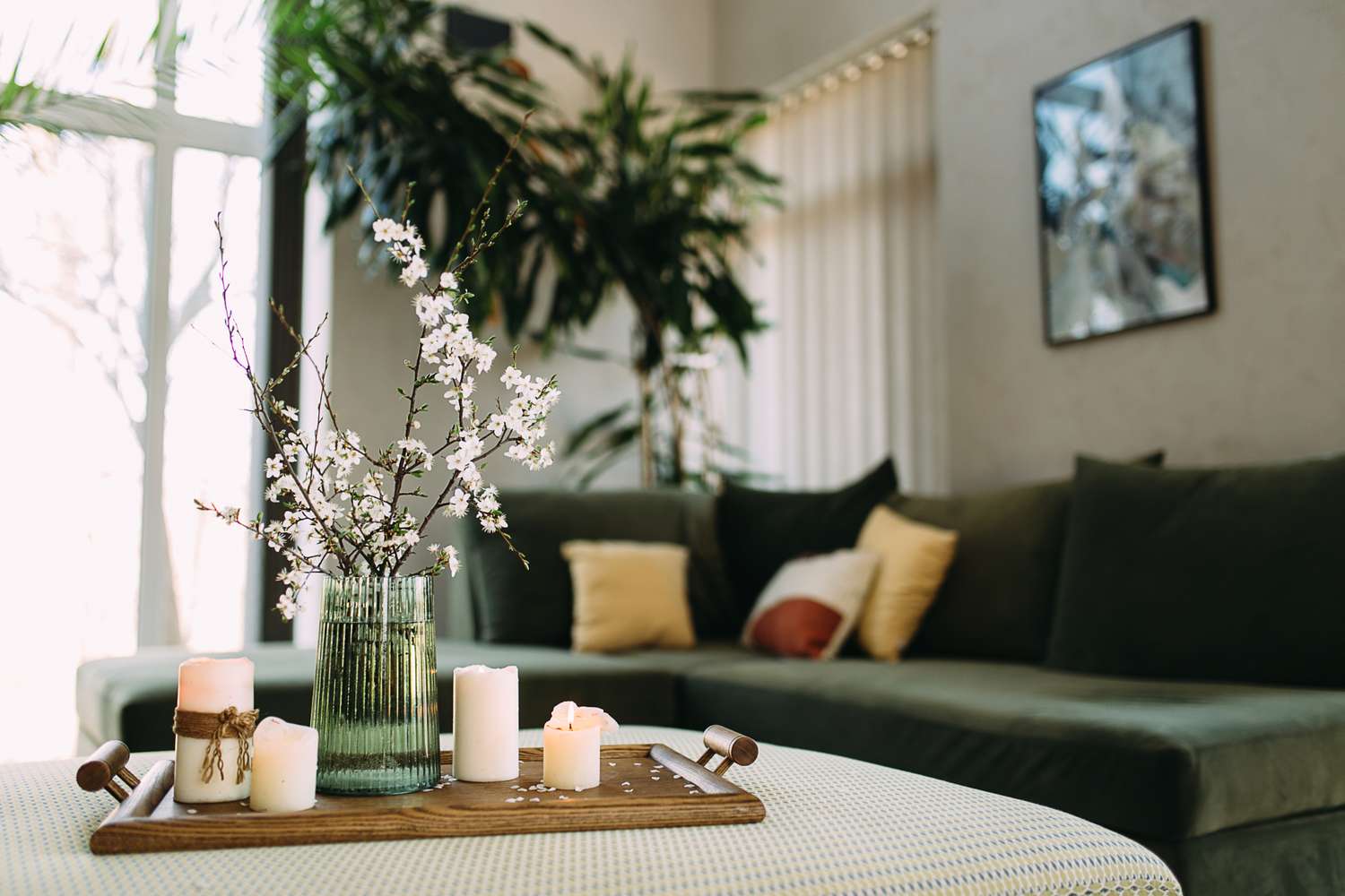 A living room with a modern sofa a wooden table centerpiece with a vase of flowers and candles on a tray