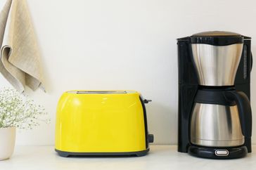 A yellow toaster and a stainless steel coffee maker on a countertop