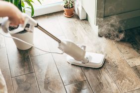 A steam mop being used on a wooden floor inside a home