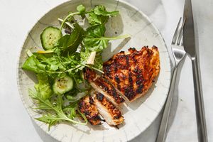 A plate with sliced grilled chicken and a mixed green salad with cucumber slices