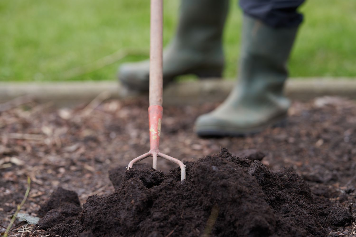 A garden fork in soil with a person wearing boots in the background
