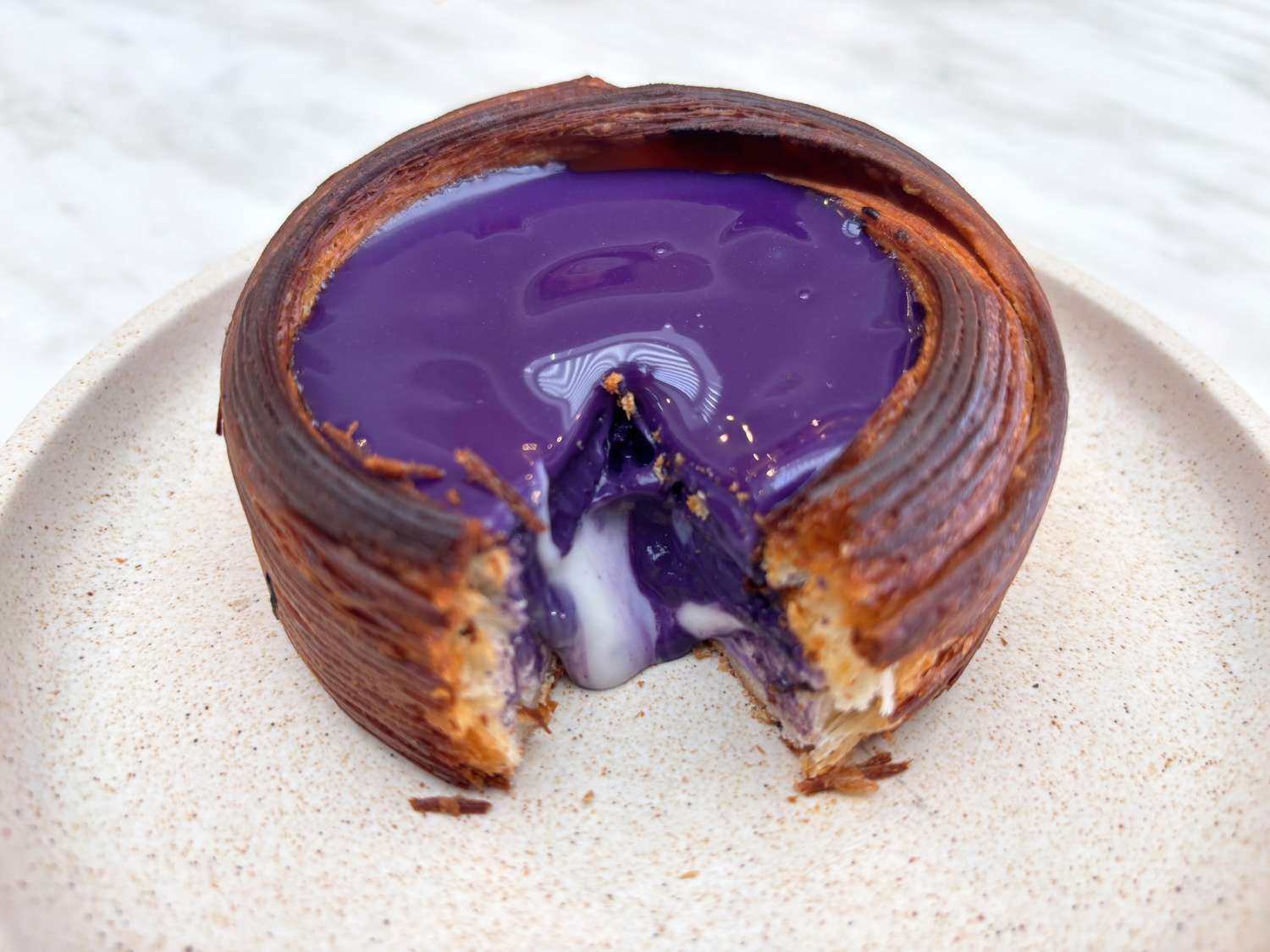 A pastry with a glossy purple filling partially eaten on a plate