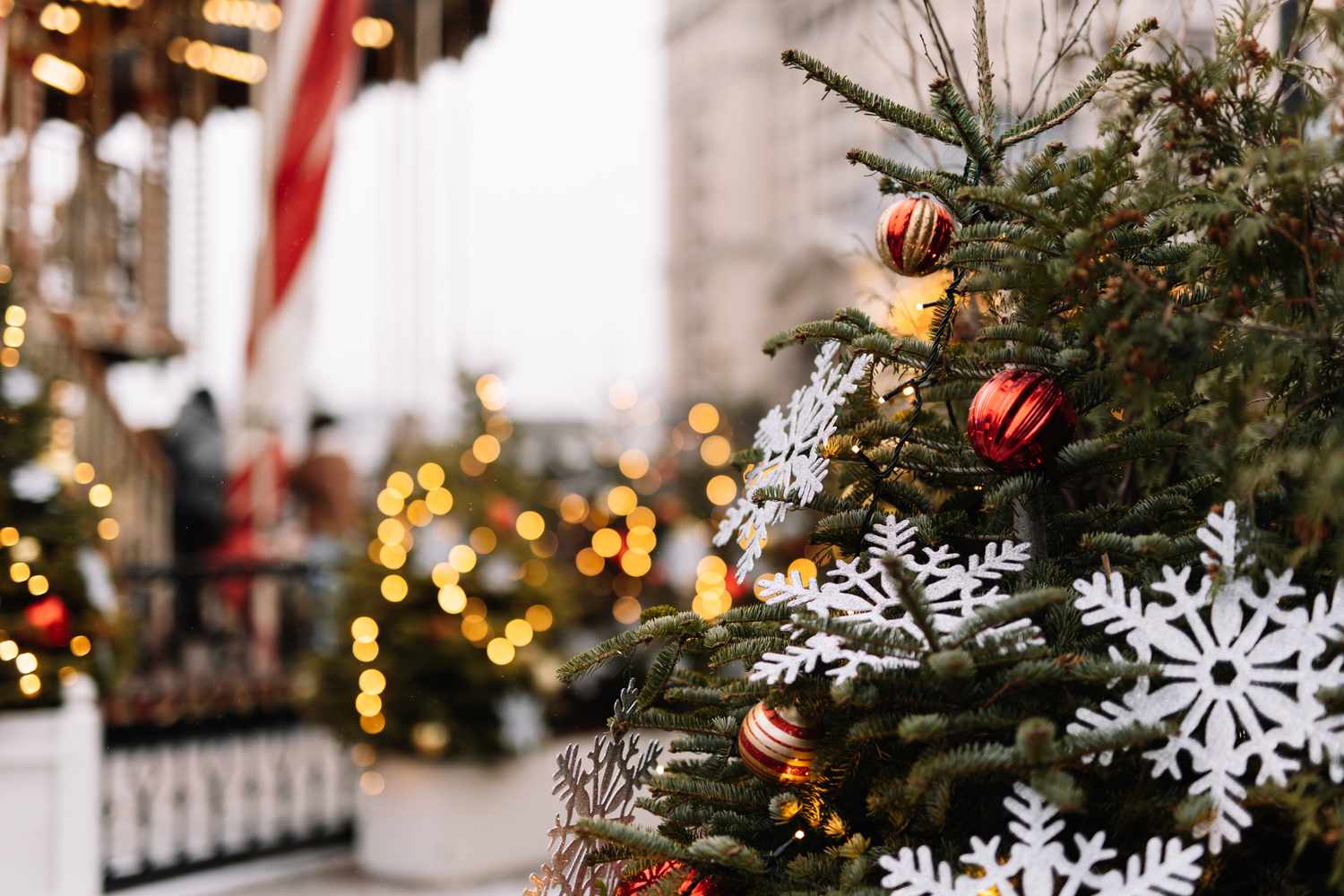 Christmas decorations on a tree including snowflakes and ornaments with festive lights in the background