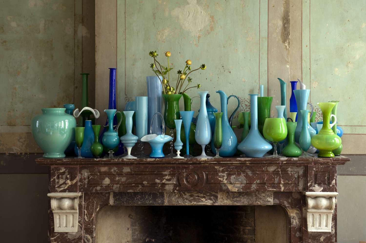 Collection of blue and green glass vases placed on a marble mantelpiece