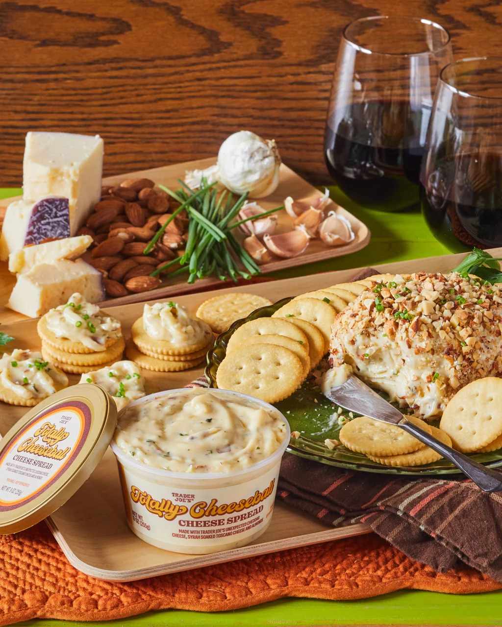 A table setting featuring cheese crackers a cheese spread container and glasses of wine in the background