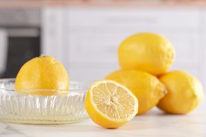 lemon being juiced in glass manual juicer and more lemons on marble counter