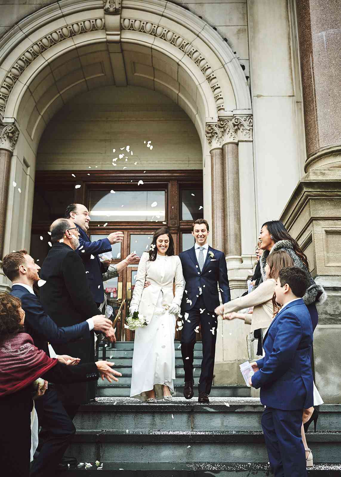 city hall wedding guests throwing flower petals at bride and groom descending staircase