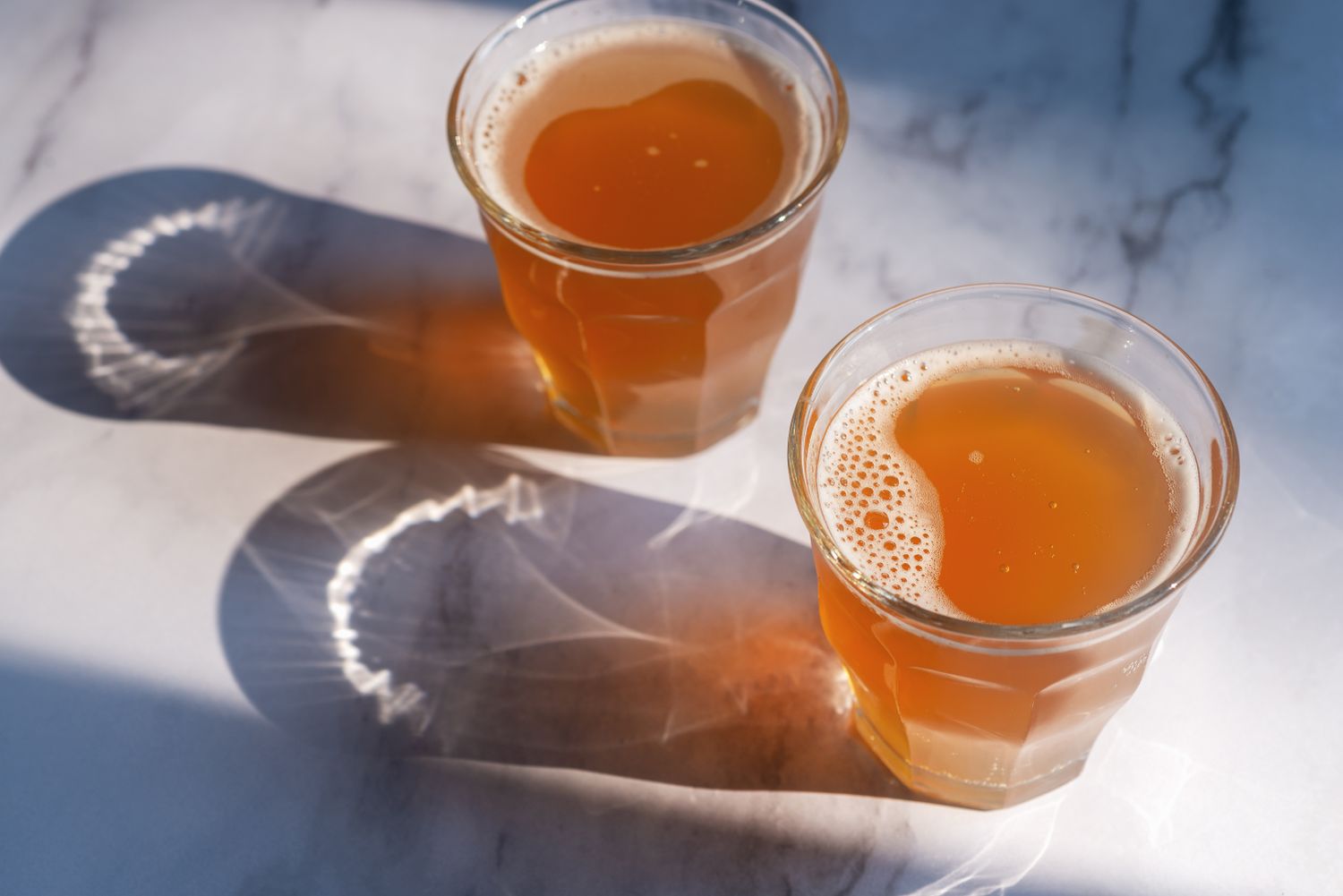 Two glasses filled with liquid on a surface casting shadows