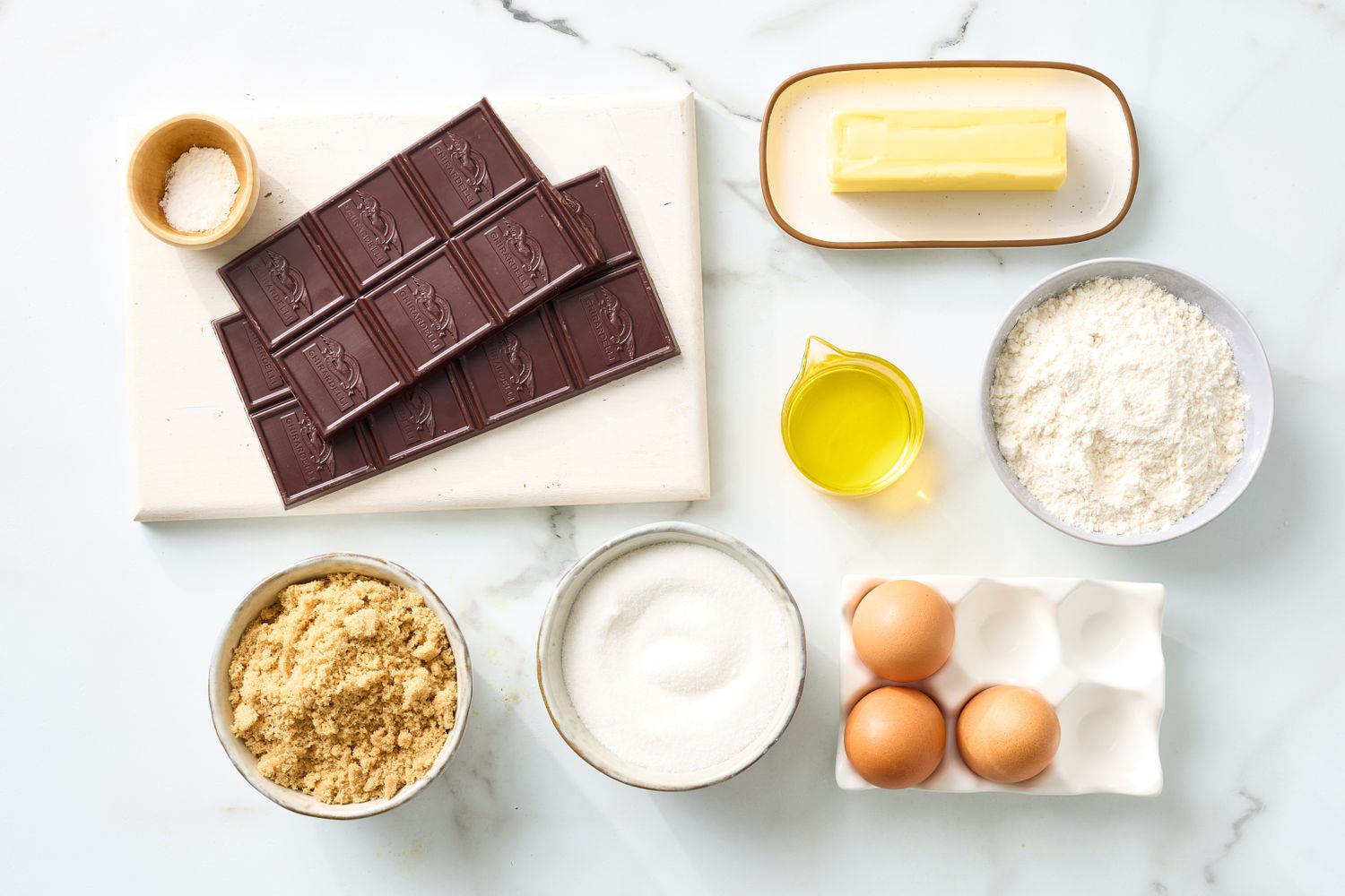Ingredients for baking including chocolate butter eggs sugar flour and oil arranged on a surface