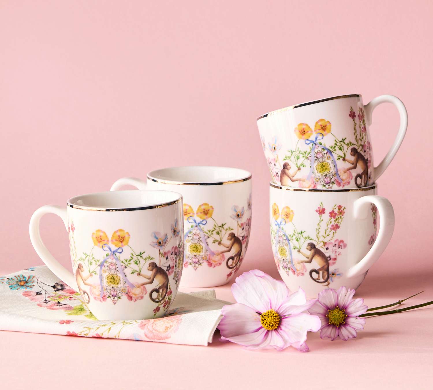 Decorative mugs with floral and leafy designs, displayed with matching accessories and pink flowers
